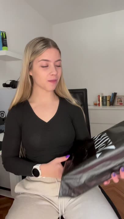 A vertical unboxing ad: a creator at her desk talks to camera, then lifts the brand's black wordmark bag and opens the maroon box.